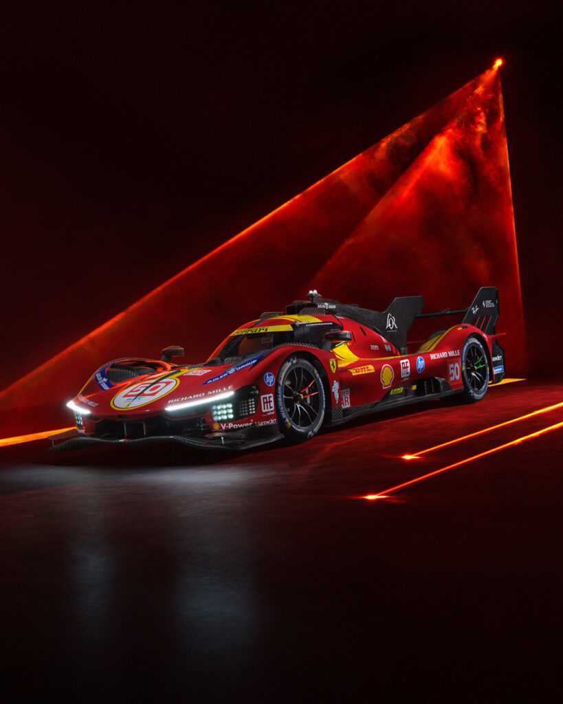A red and black Ferrari racing car, the 499P with the number 50, is displayed in a studio with red laser lights shining on it.