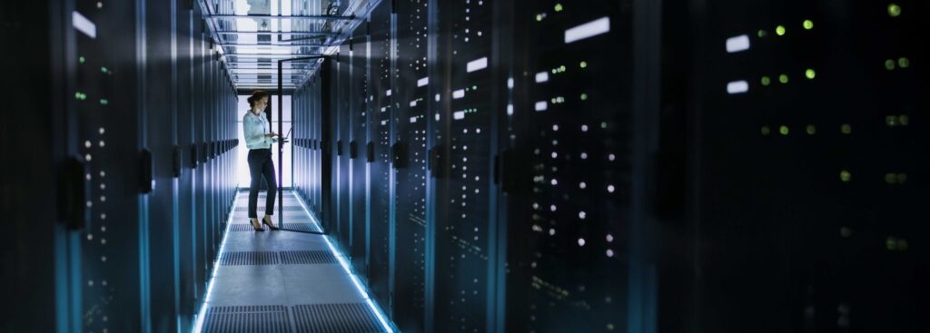 Female engineer in data center hallway illuminated with servers and blue LED lights